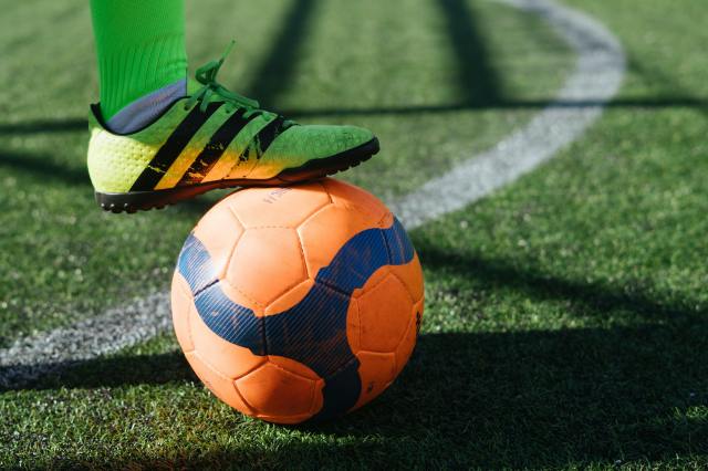 Image of green cleat on top of an orange soccer ball on soccer turf field